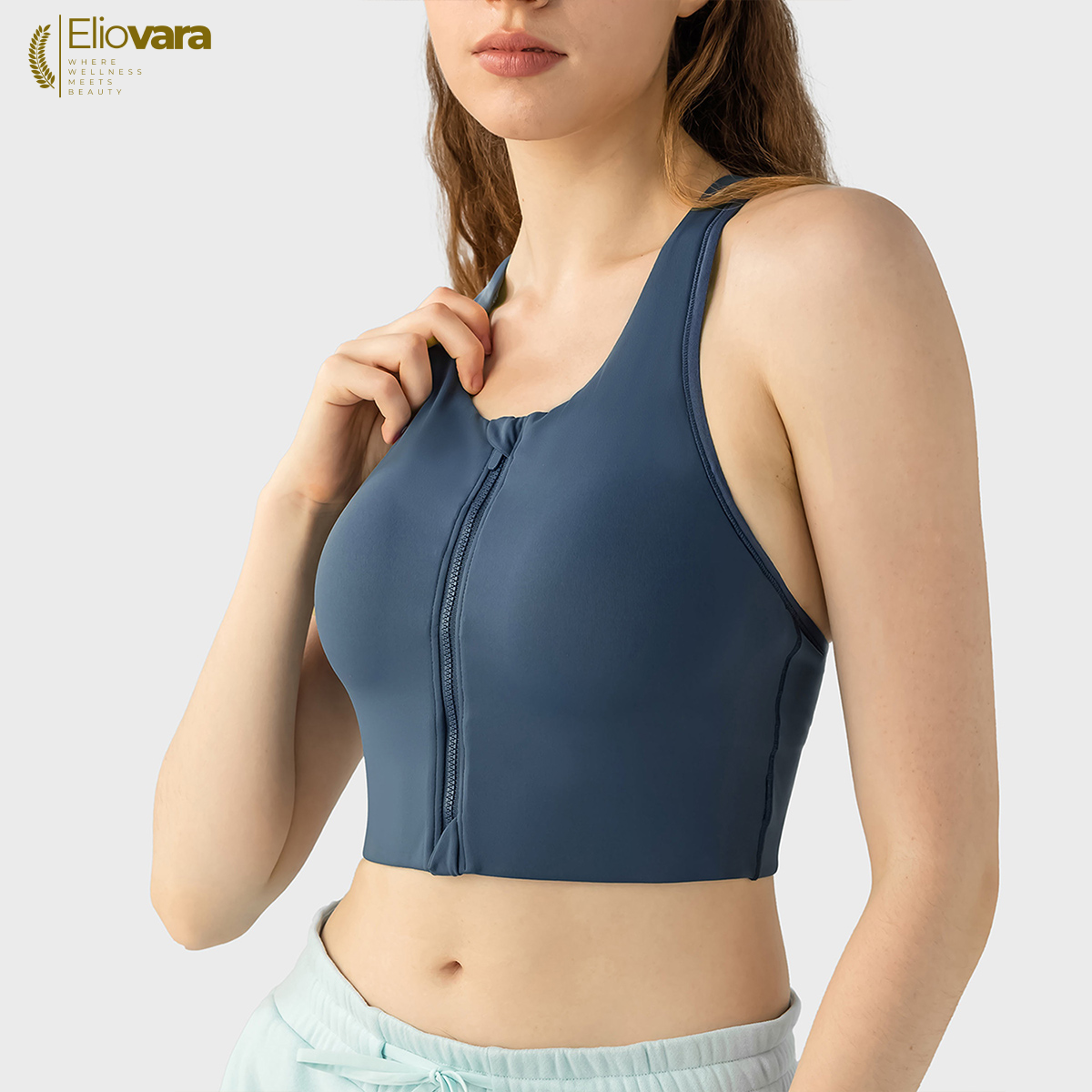 Woman wearing a blue sports bra with a plain background, featuring the Eliovara brand.
